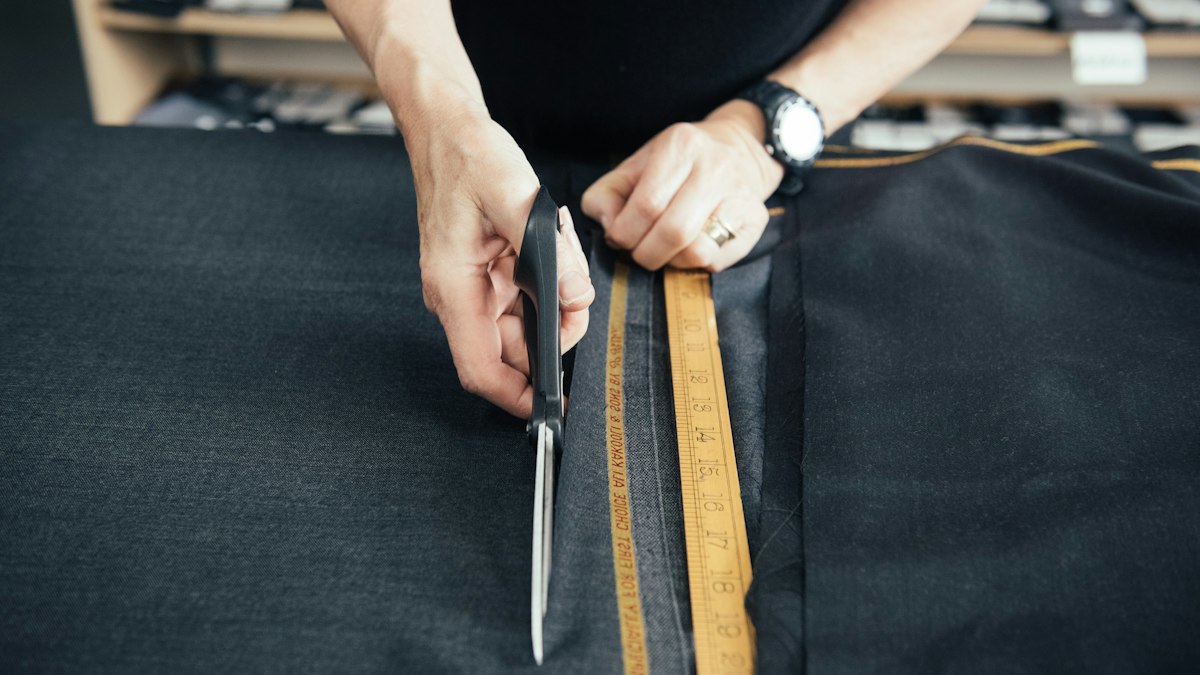Портной раскраивает ткань ножницами по линейке